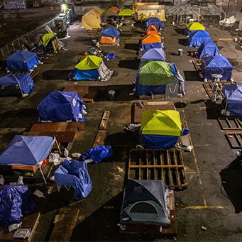 photograph of several rows of tents in a fenced lot that is housing the homeless.